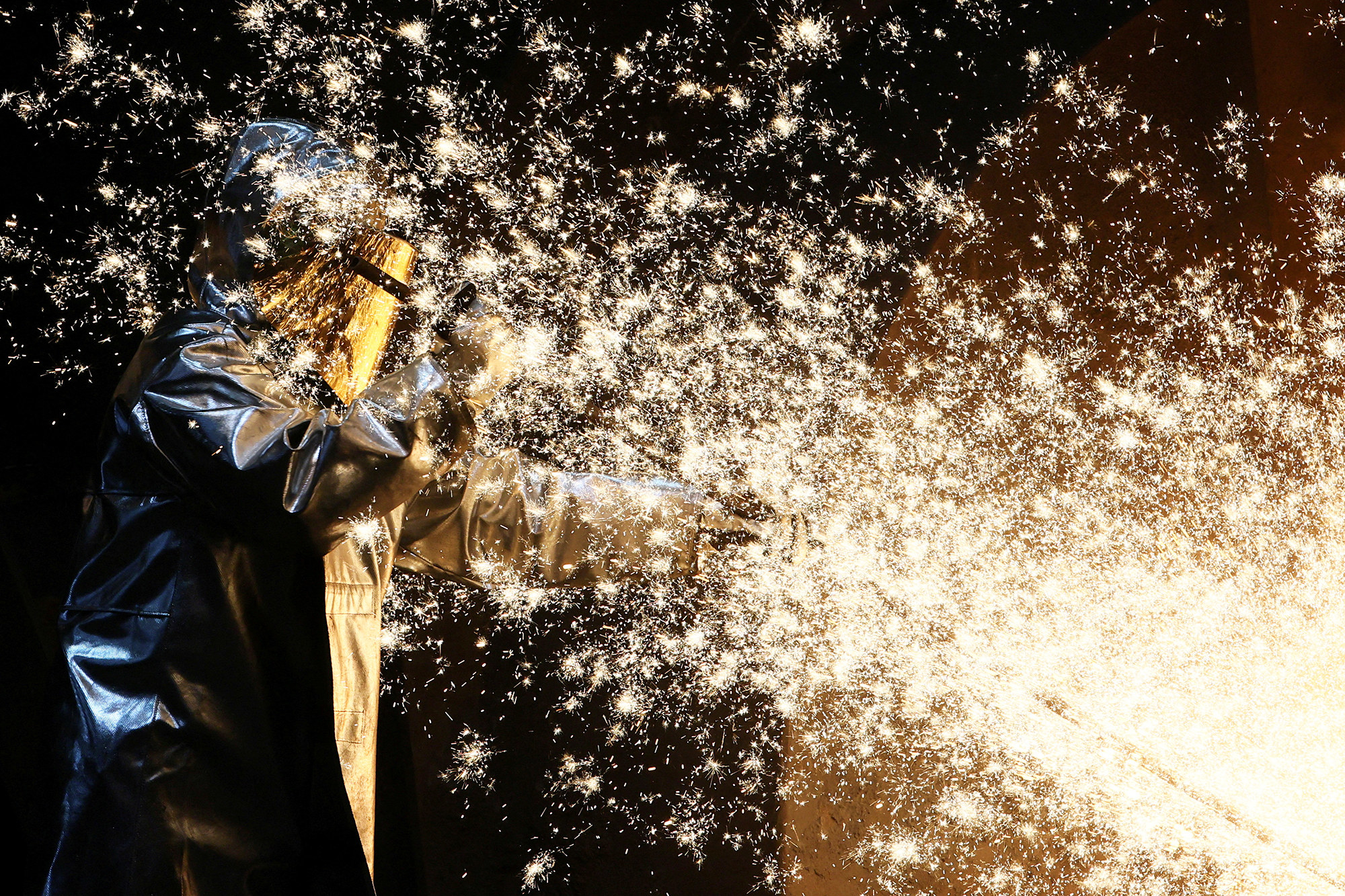 a flurry of golden sparks shower a masked steel worker