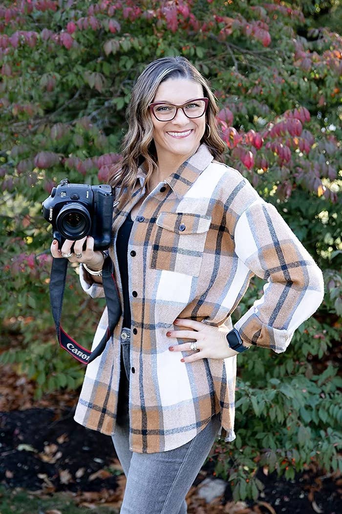 A reviewer wearing a brown and blue shacket with a camera and light was jeans