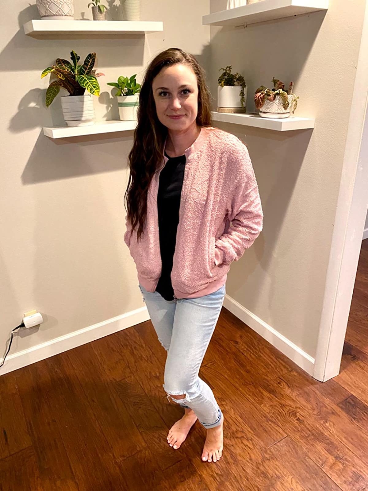 A reviewer wearing a black top, pink jacket and light wash denim