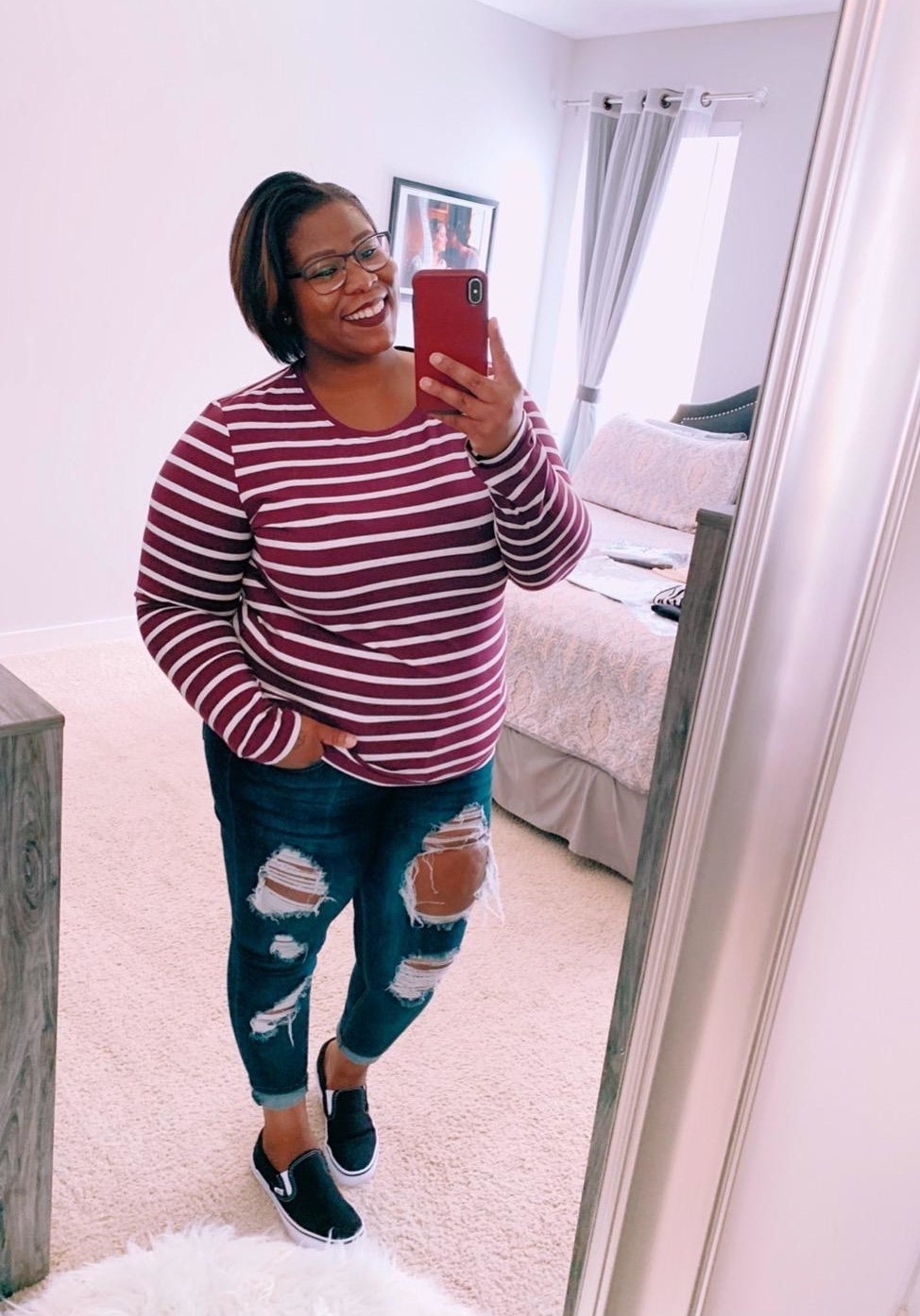 A reviewer wearing red and white tee with jeans and slide on sneakers