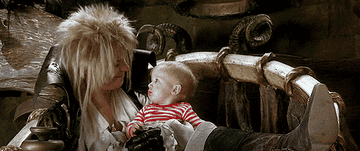 david bowie sits with a baby in costume in the film labyrinth
