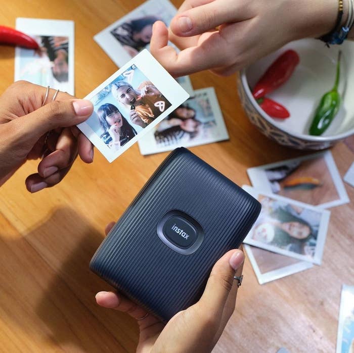 a person holding the instax printer surrounded by various instantly printed photos