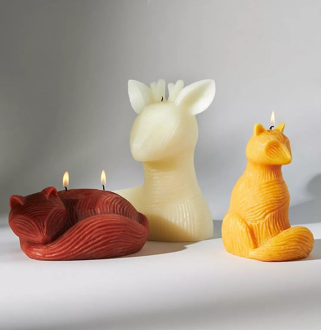 A white deer candle, a yellow sitting fox candle, and a red sleeping fox candle