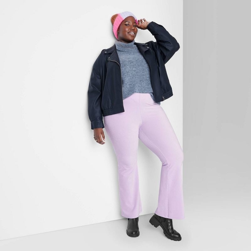 Model wearing purple velour pants with gray shirt, black jacket, and pink beanie
