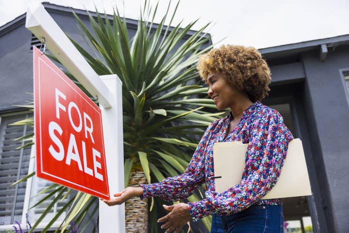 Realtor hanging a For Sale sign in front of a house