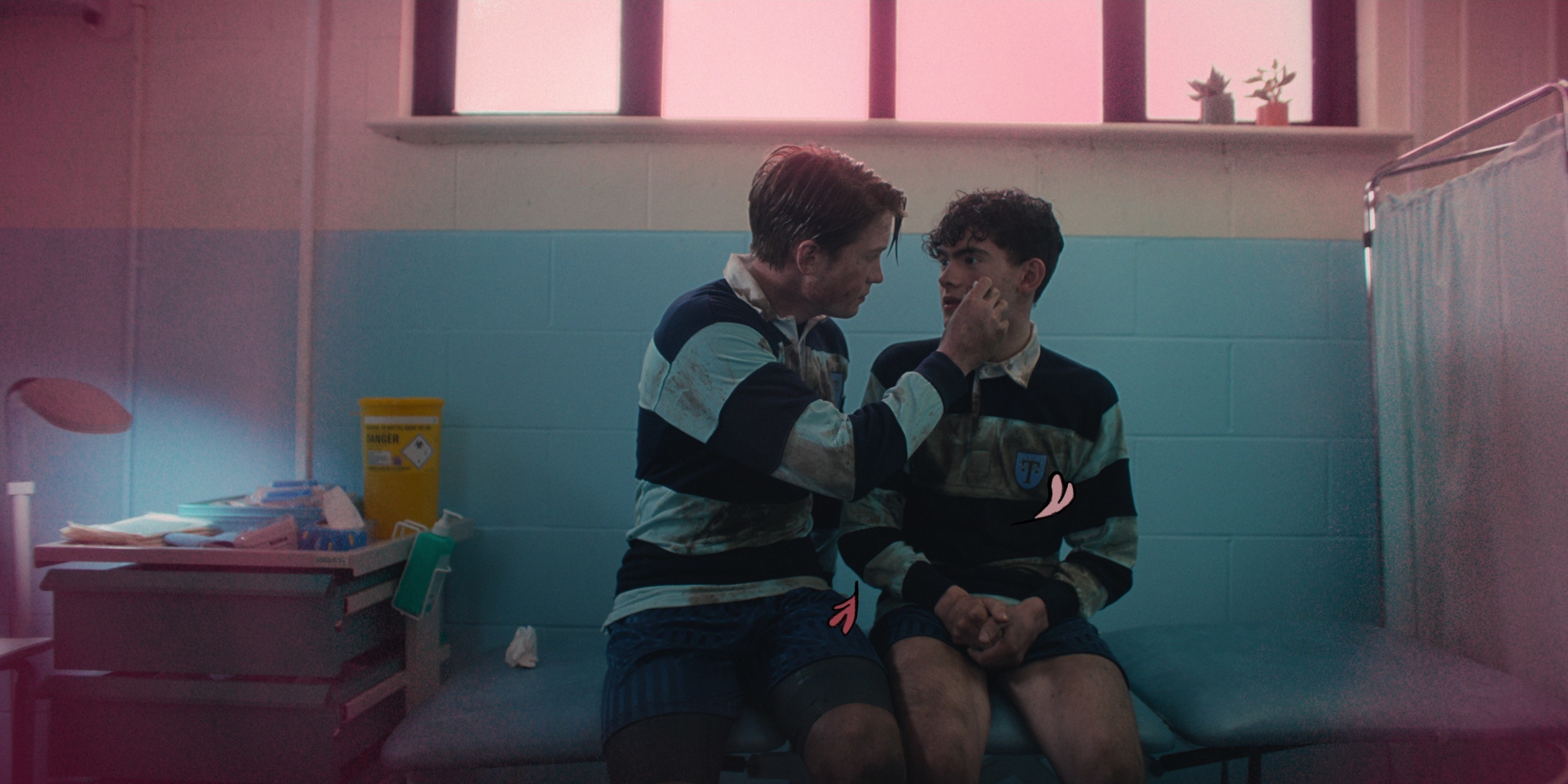 Kit Conner and Joe Locke sit close to each other in a nurse&#x27;s office in Heartstopper. They wear rugby uniforms.