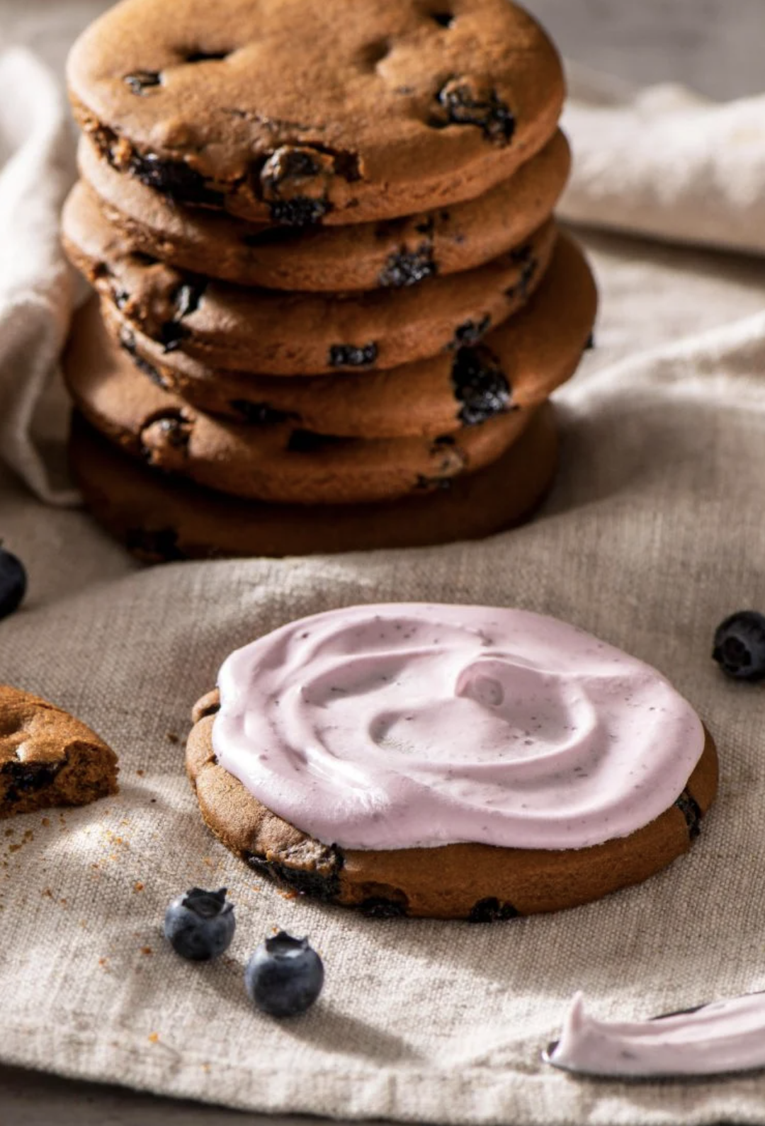 One frosted blueberry gingerbread cookie sits in front of a stack of unfrosted cookies