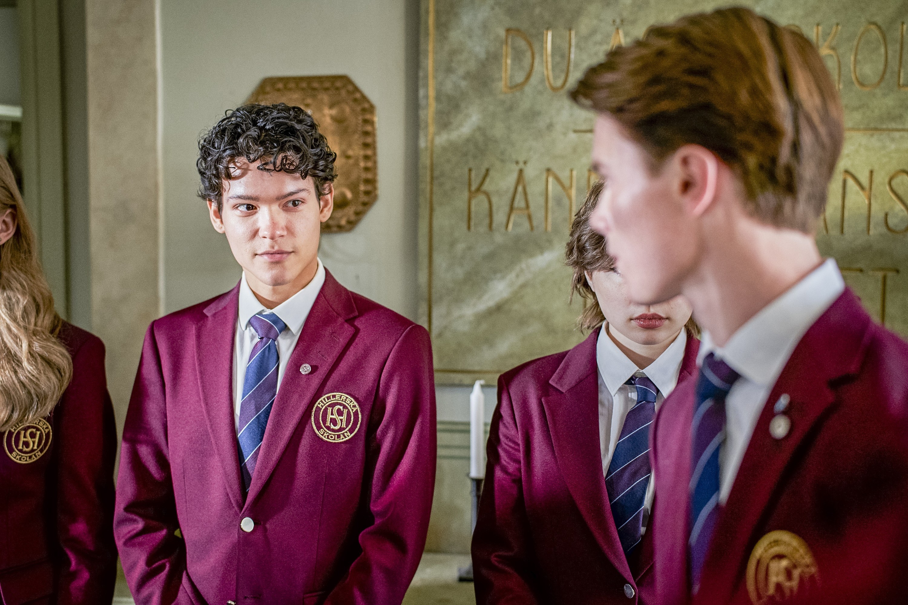 Omar Rudberg and Edvin Ryding look at each other in Young Royals. They both wear school uniforms.