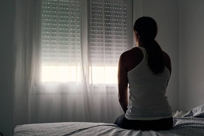 A woman sitting on her bed and staring at her window