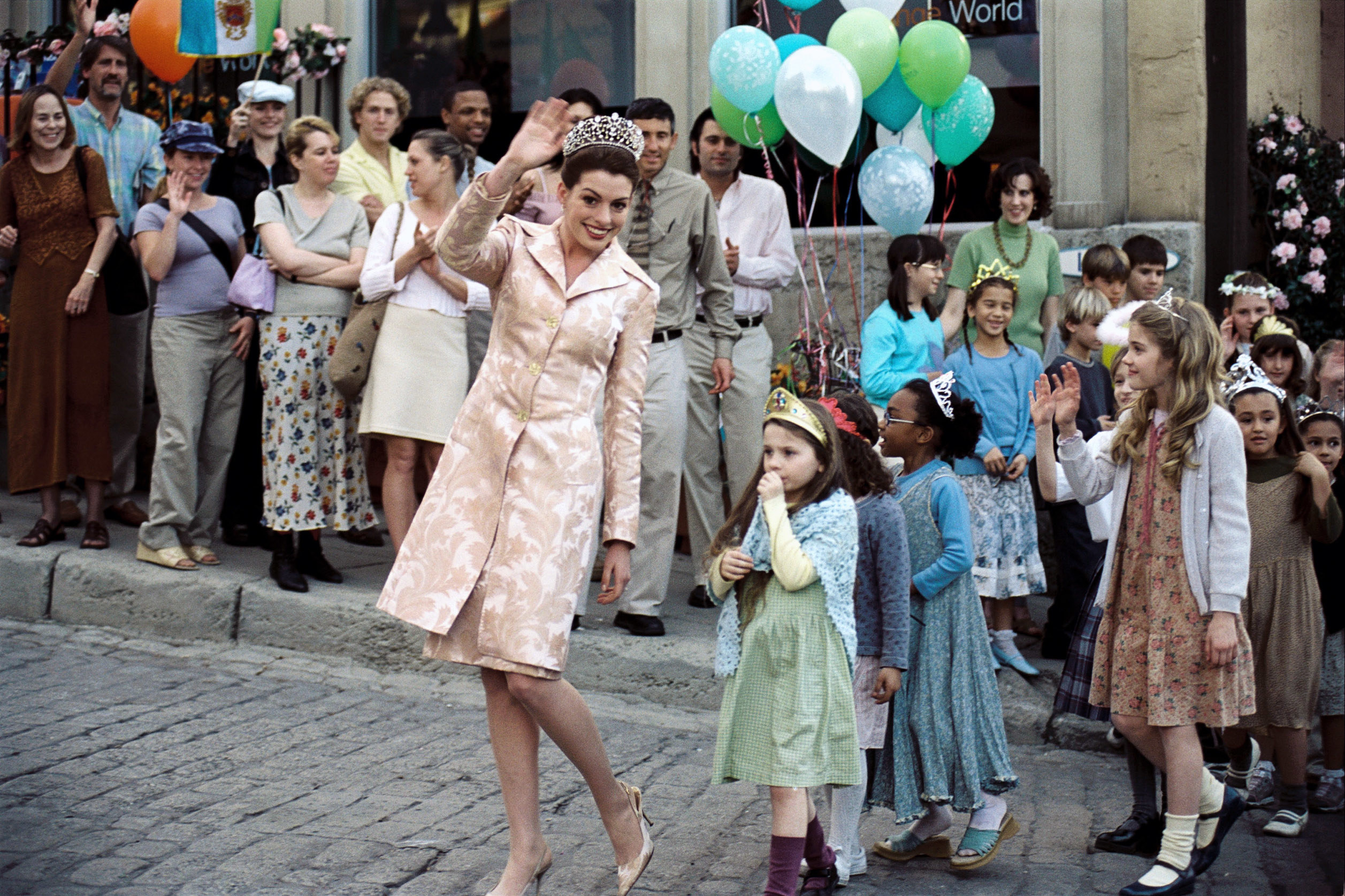 Mia wearing a tiara and leading a group of young children also wearing tiaras through a parade