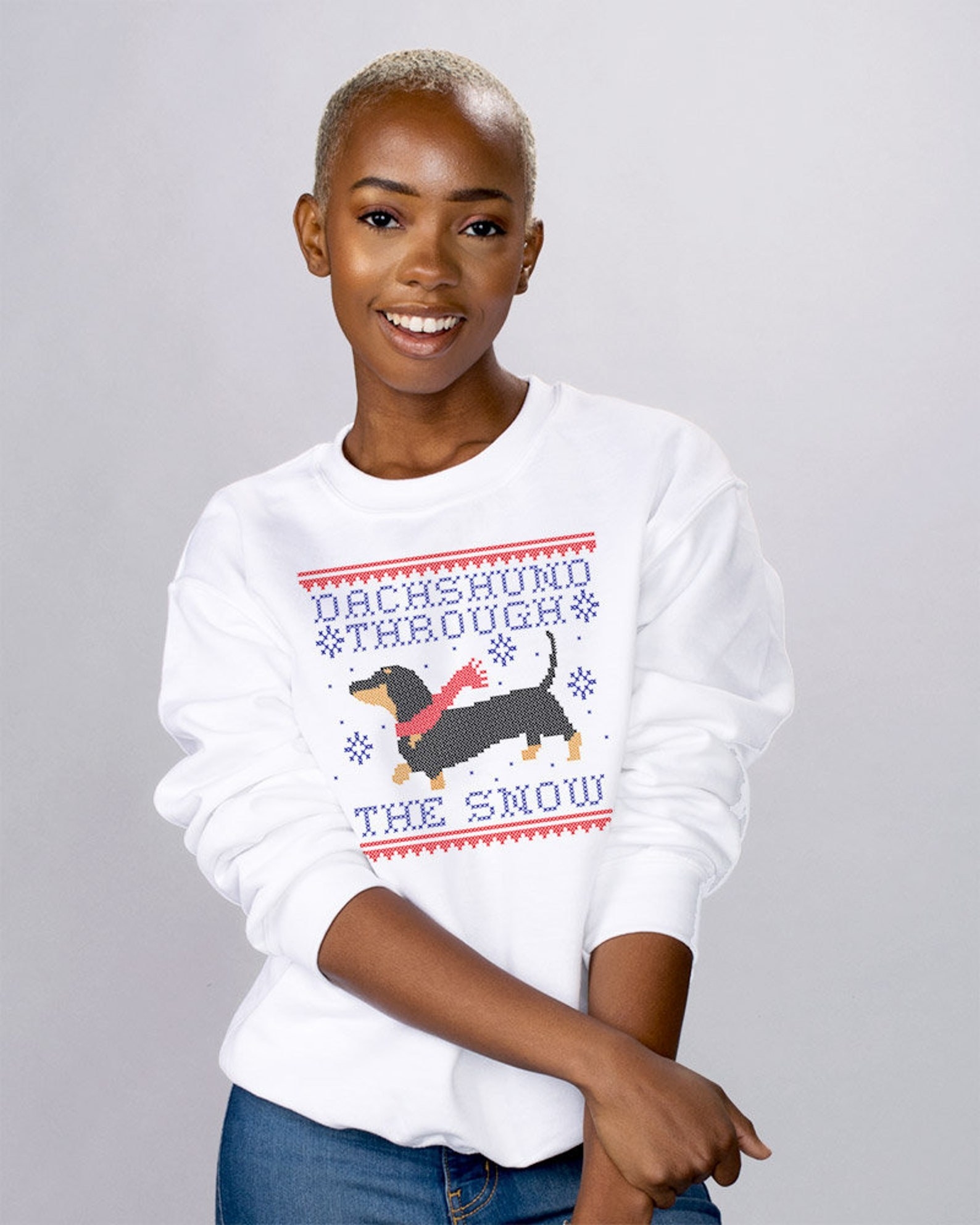 A model in the white crewneck with &quot;dachshund through the snow&quot; in cross-stitch style text and a dachshund in a red scarf