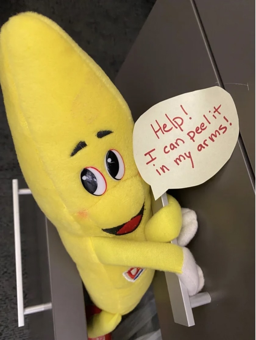 a stuffed banana toy with a sign that reads, help, i can peel it in my arms