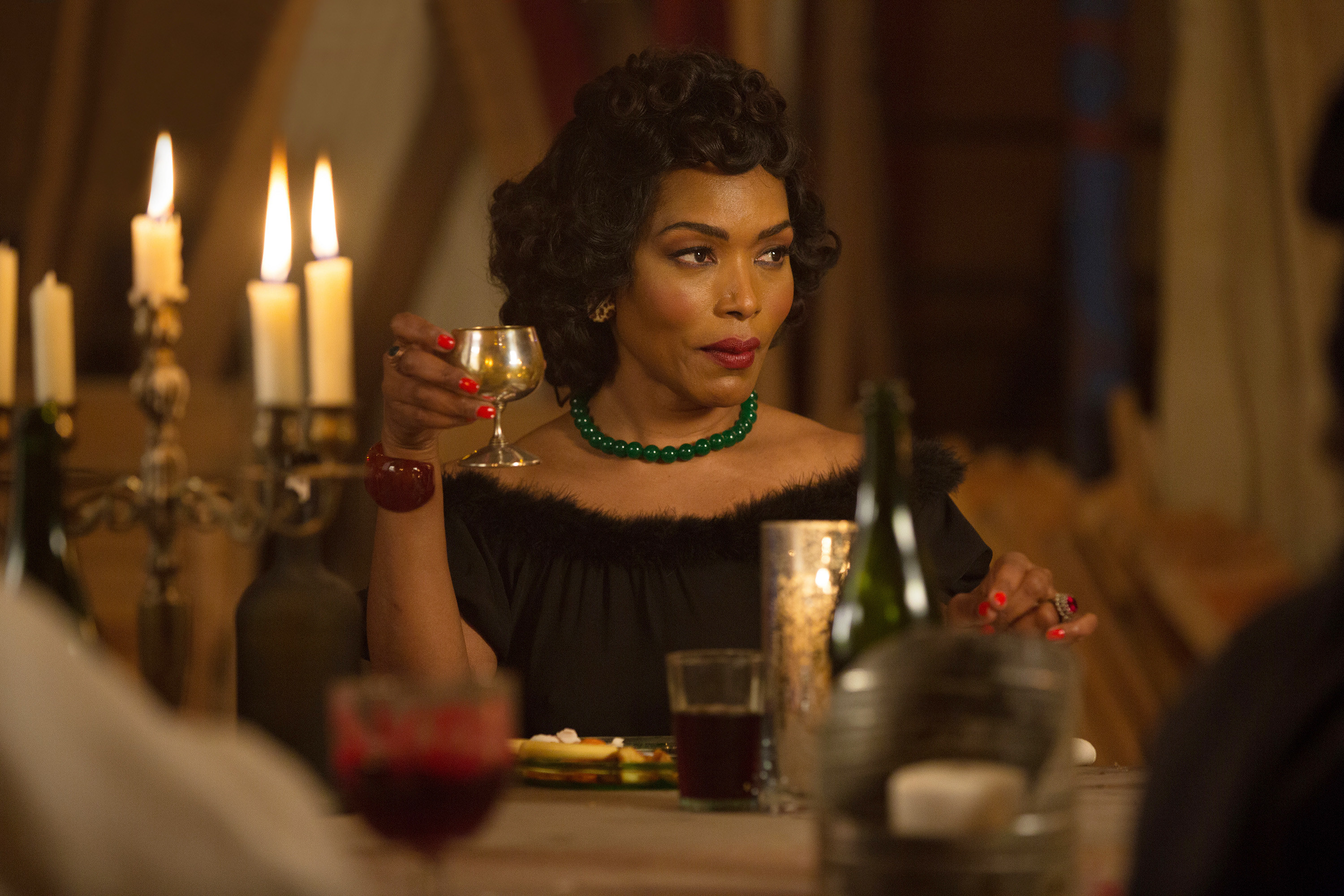 Angela Bassett holding a drink and sitting at a table in American Horror Story: Freak Show