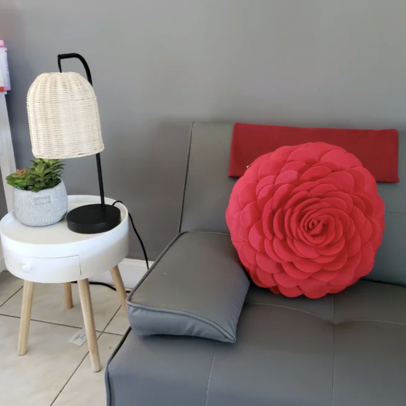 reviewer&#x27;s photo of the red round floral throw pillow resting on grey couch
