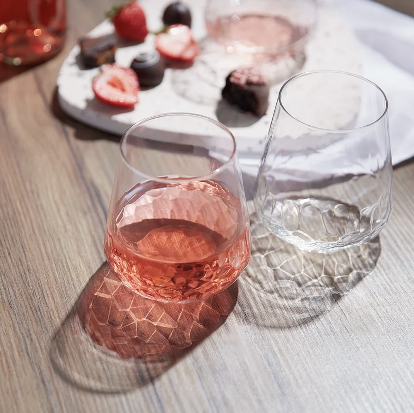 Two of the glasses on table, one filled with rose wine and giving off unique pattern