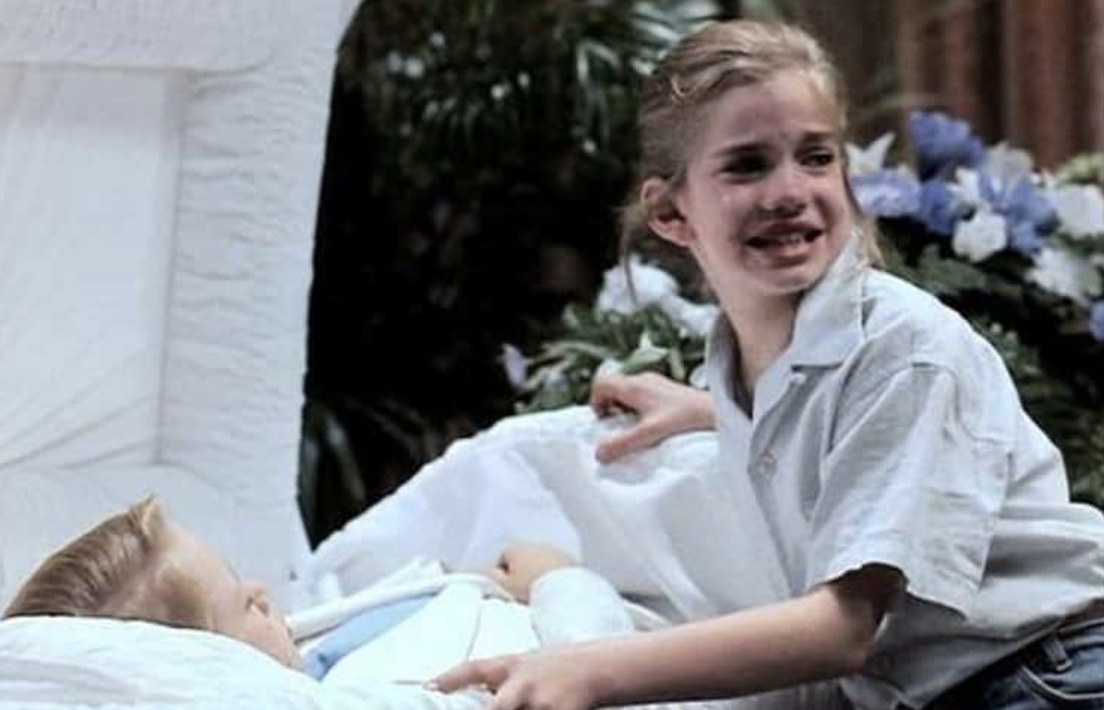 a girl crying over a little boy in a casket
