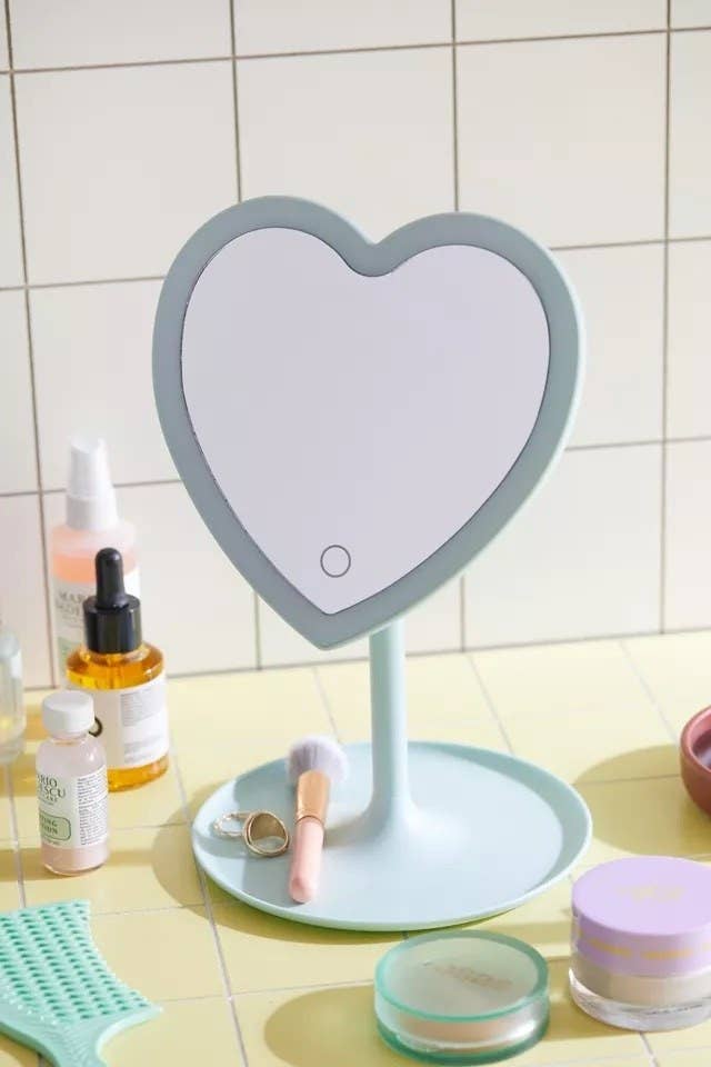 the heart shaped makeup mirror on a bathroom counter surrounded by beauty products