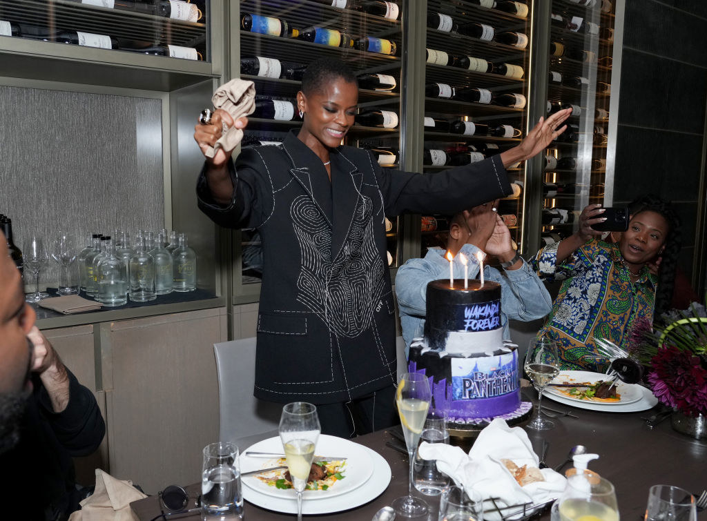 Letitia standing in front of  Wakanda Forever birthday cake at a restaurant table with people sitting around it