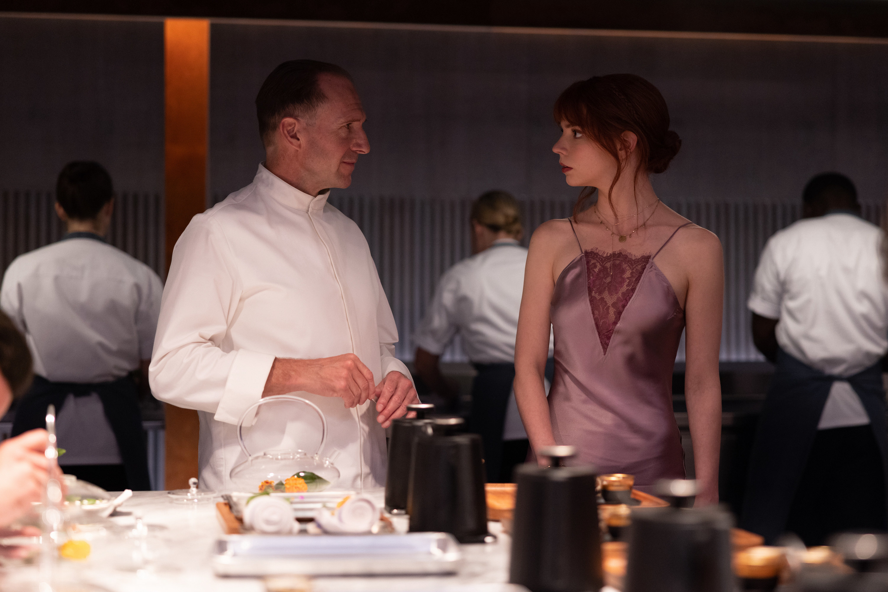 Ralph Fiennes and Anya Taylor-Joy look at one another in a kitchen