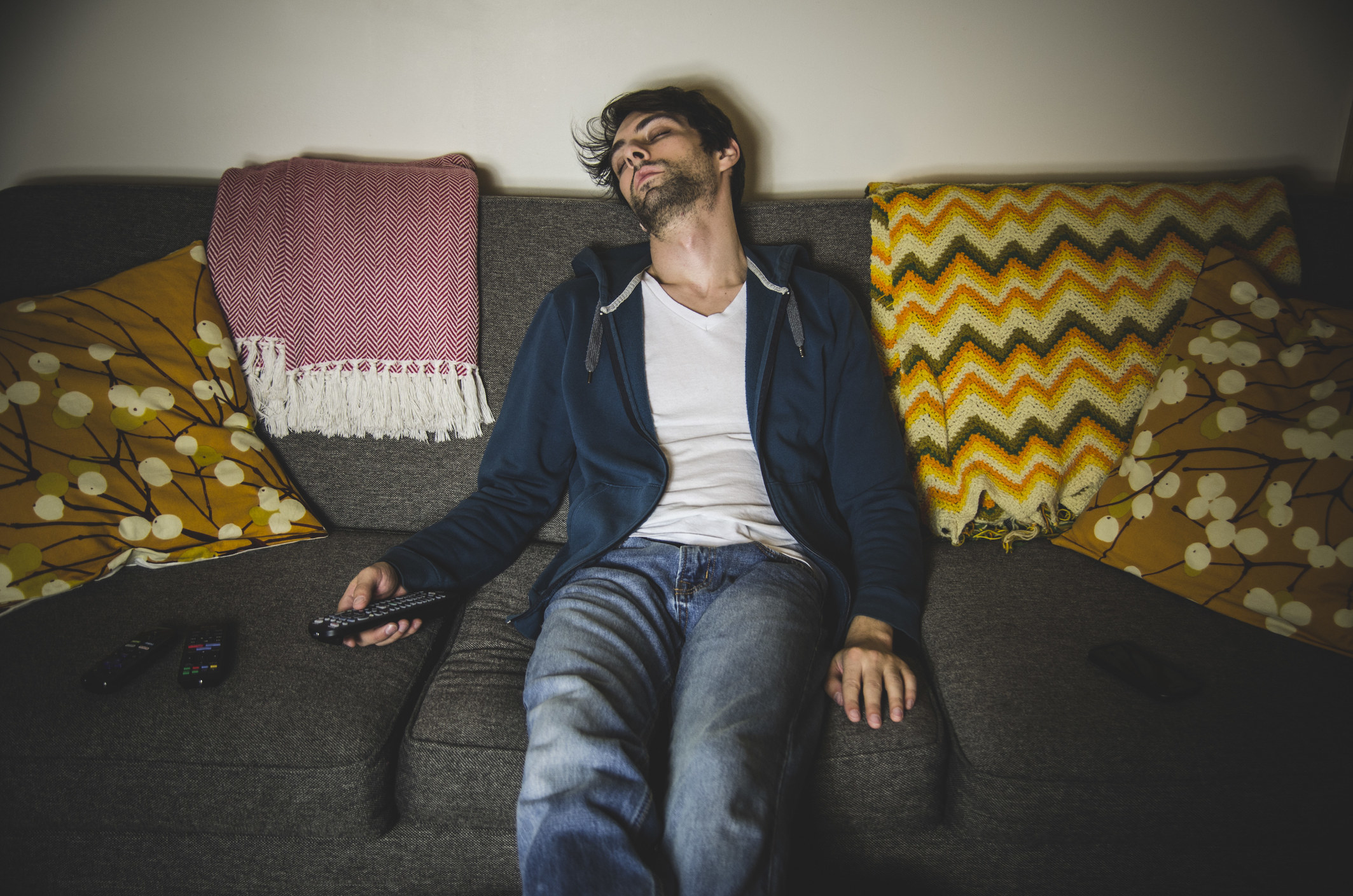 A man sleeping on the couch with the television remote in his hand
