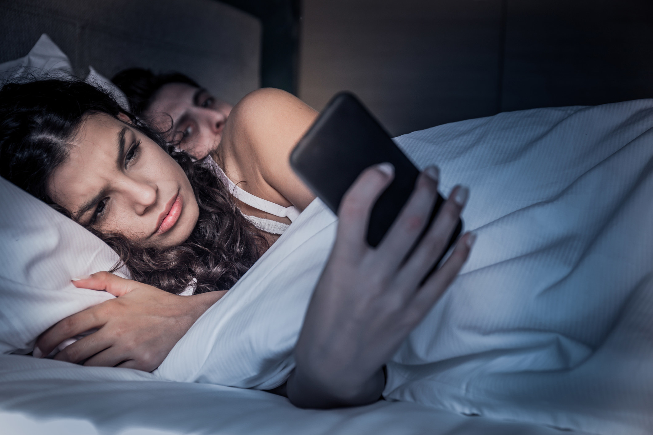Woman on her phone in bed beside partner