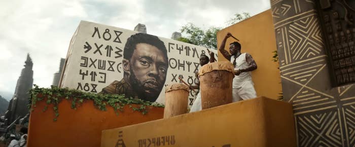 An mural of T&#x27;Challa alongside men beating drums on a platform