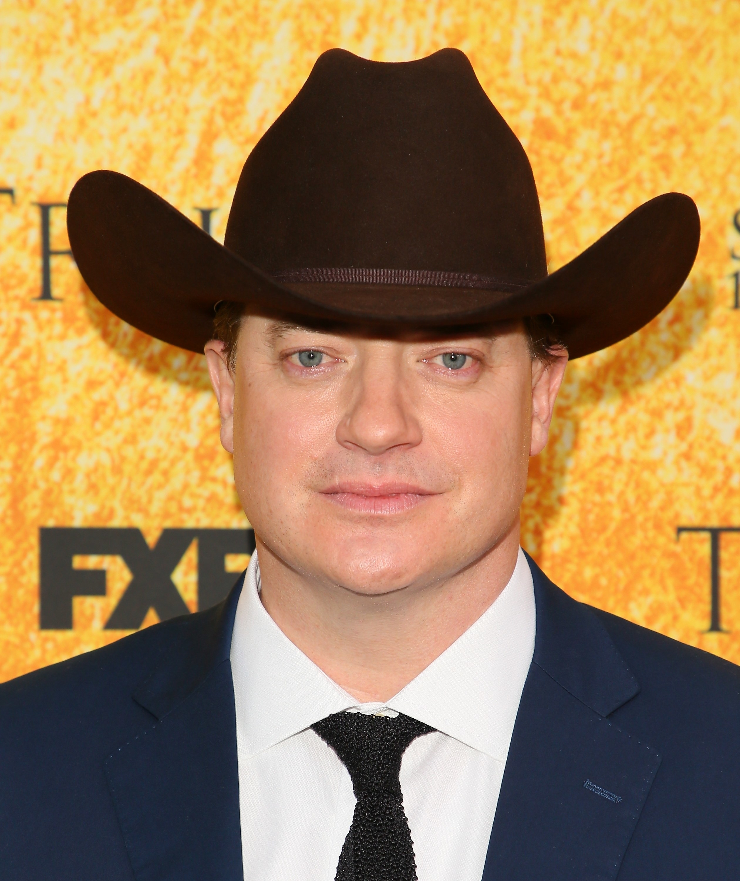 A closeup of Brendan Fraser wearing a cowboy hat and suit and tie at a red carpet event