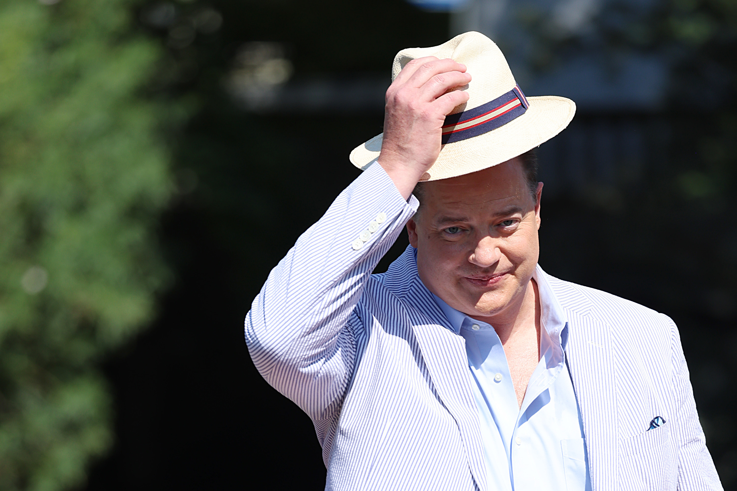 Brendan Fraser walking outside while adjusting his fedora