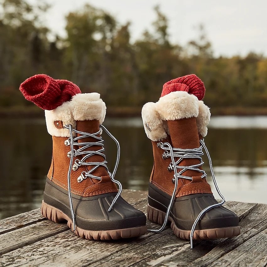 Tan boots with black front and sherpa upper lining on the dock in front of a lake