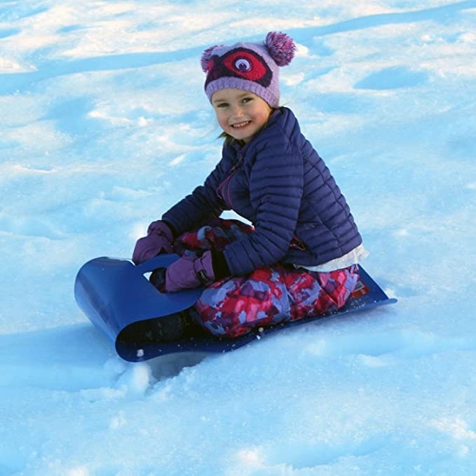 Child going down snowy hill with flexible blue roll-up sled