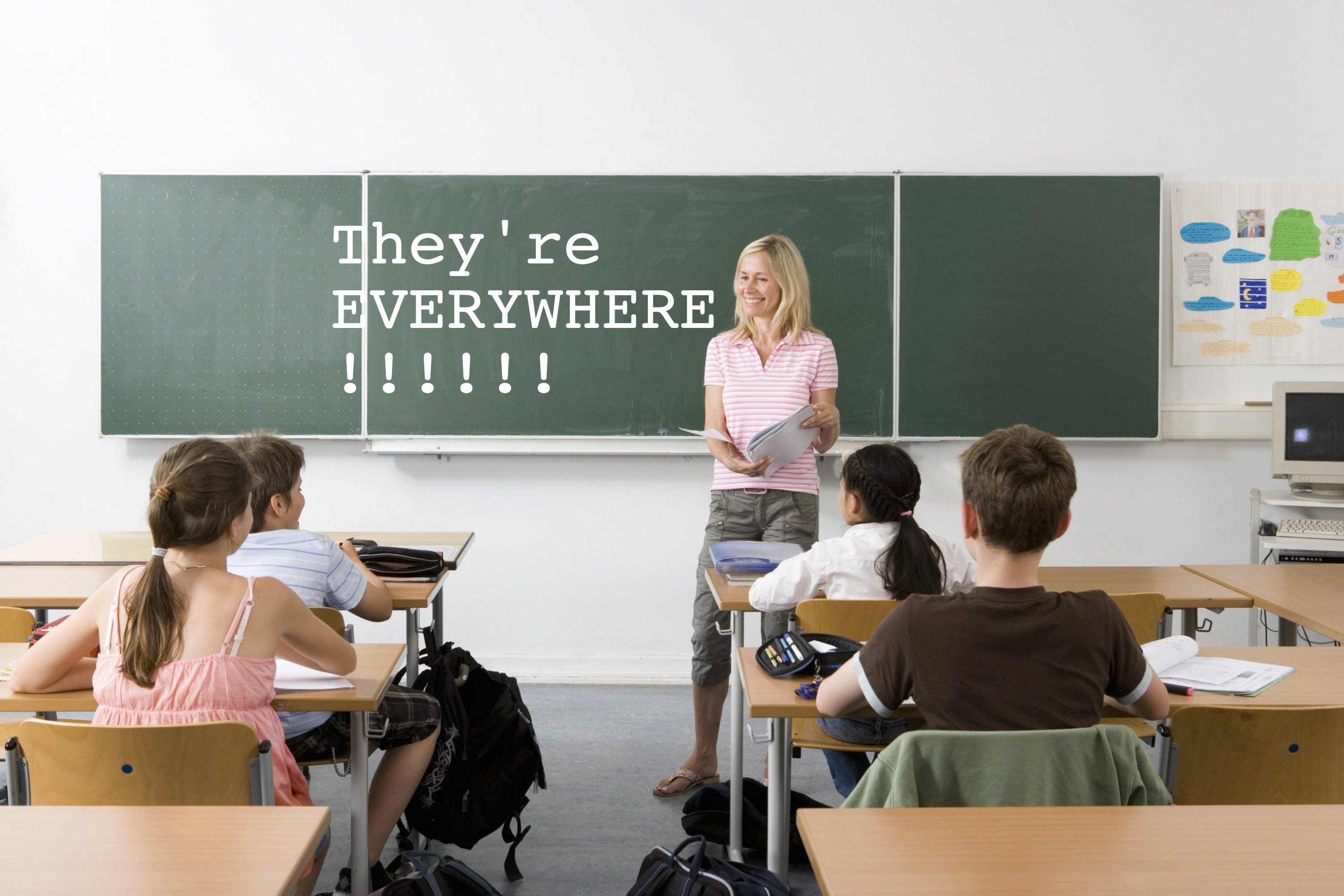 A teacher standing at the front of a class with &quot;They&#x27;re EVERYWHERE!!!!!!&quot; written on the chalkboard
