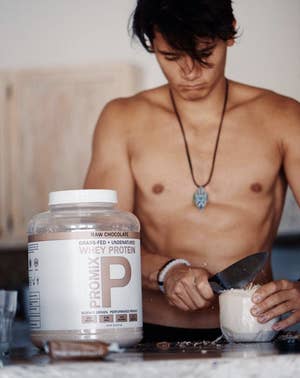 Someone cutting open a coconut next to a giant container of protein powder