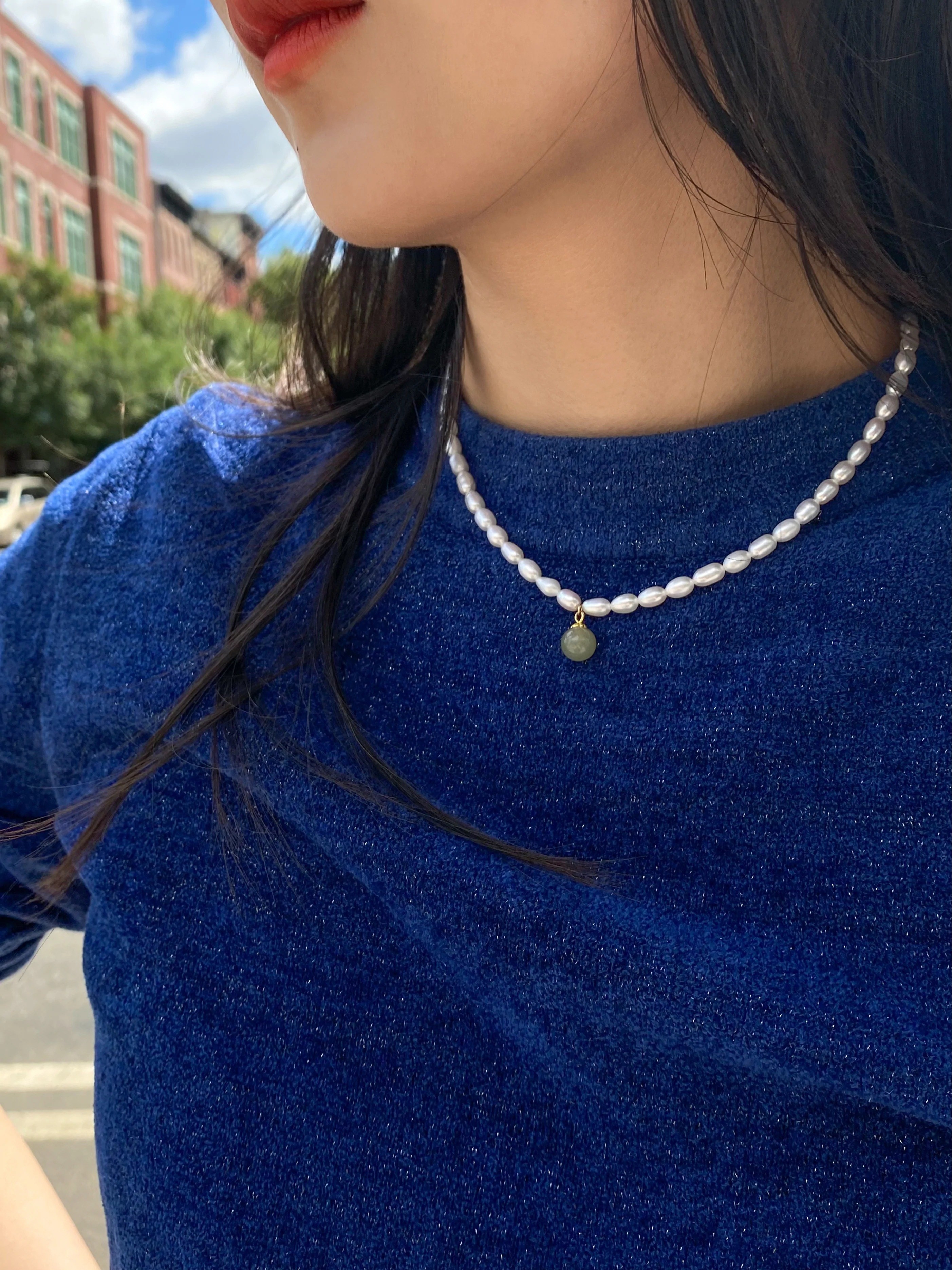 Model wearing blue shirt and pearl choker with green jade attached.