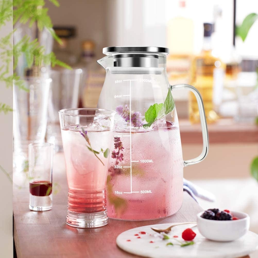 the pitcher filled with flowers and mint with a glass next to it and the garnishings next to it