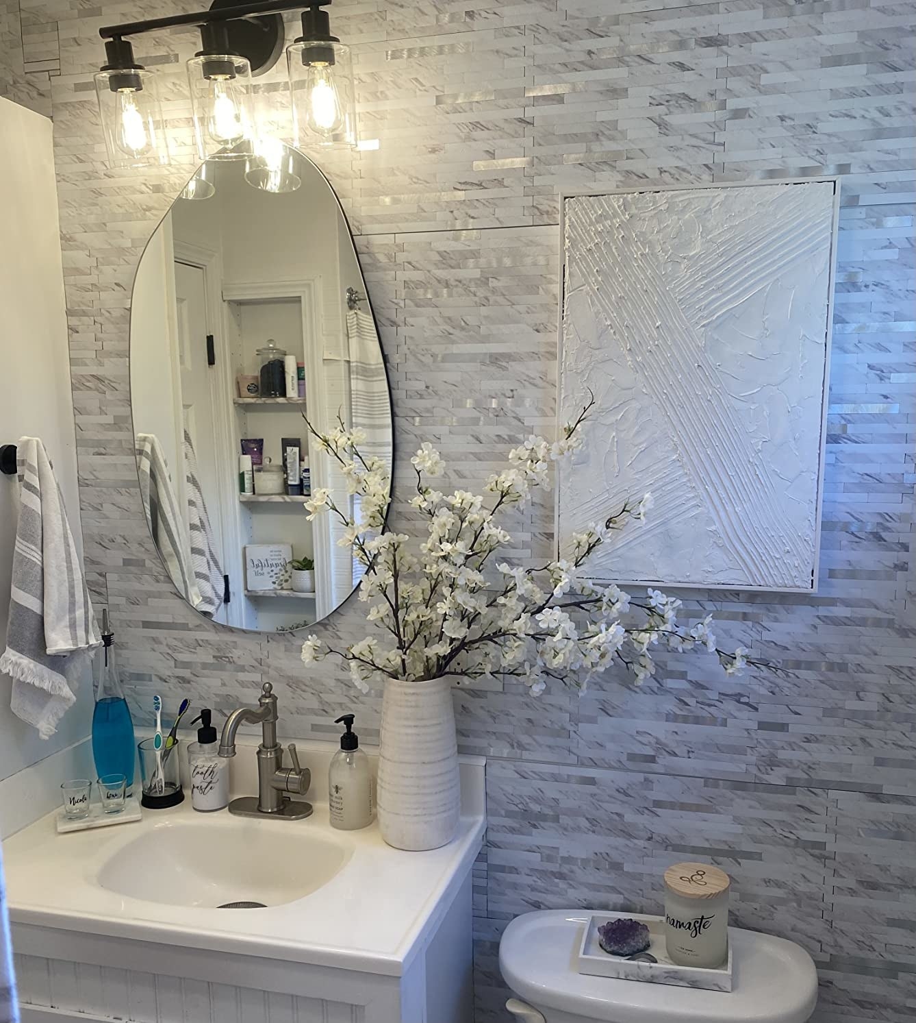 a reviewer photo of the black light fixture in a decorated white and grey bathroom