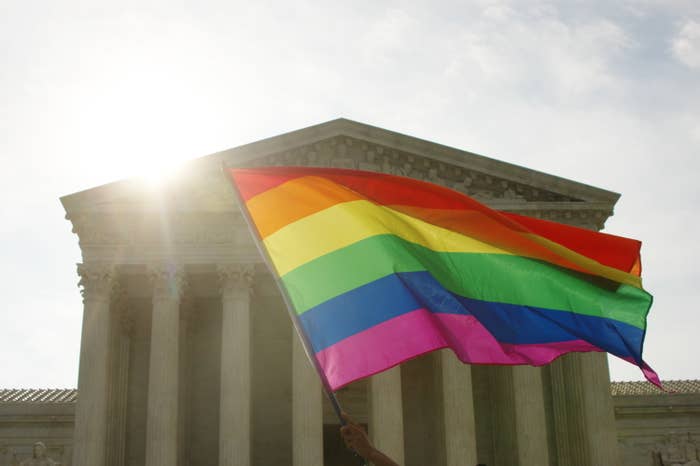 A pride flag is waved in front of the United States Supreme Court, behind which the sun sets