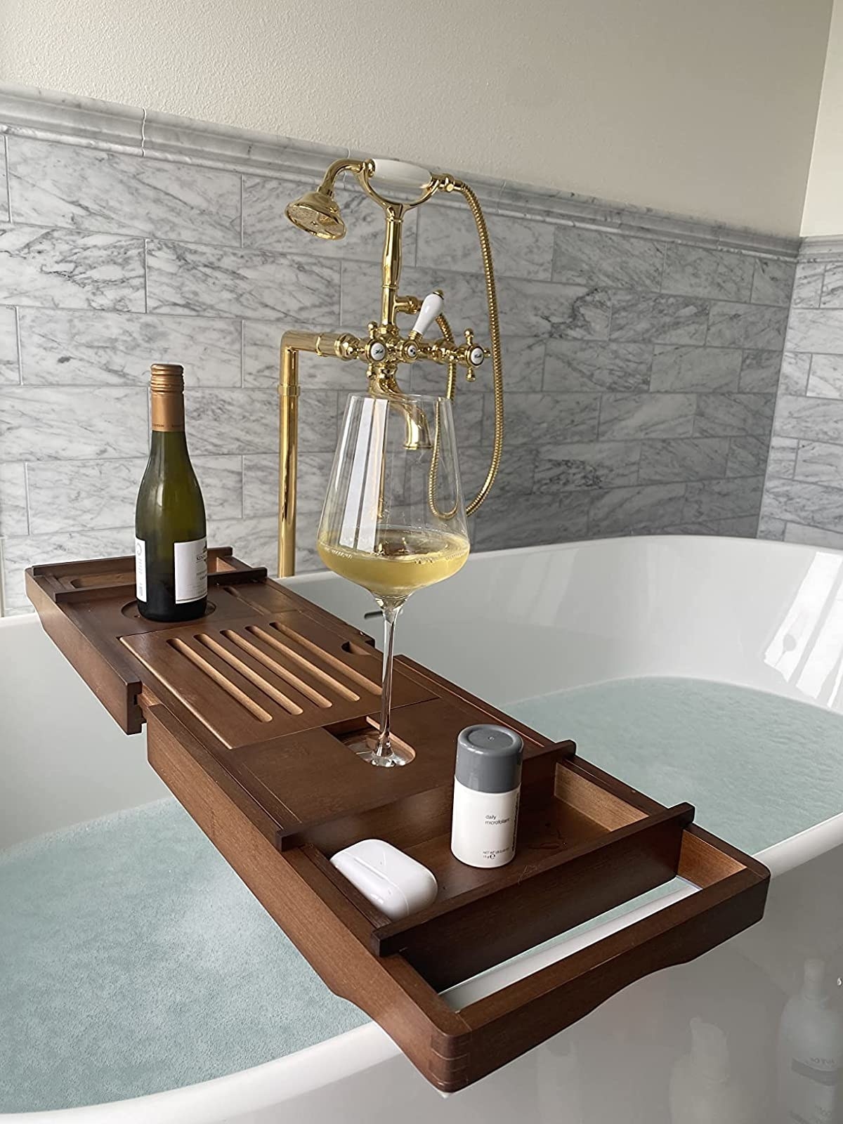 a reviewer photo of the dark wood tray with wine and toiletries across a large white tub