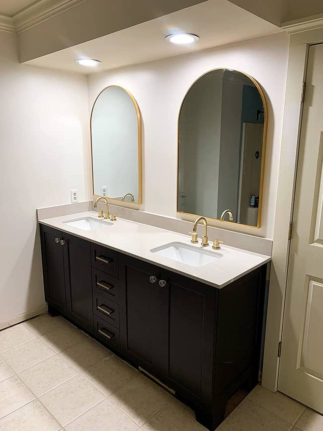 a reviewer's two gold-edged arched mirrors hanging above a dual sink vanity