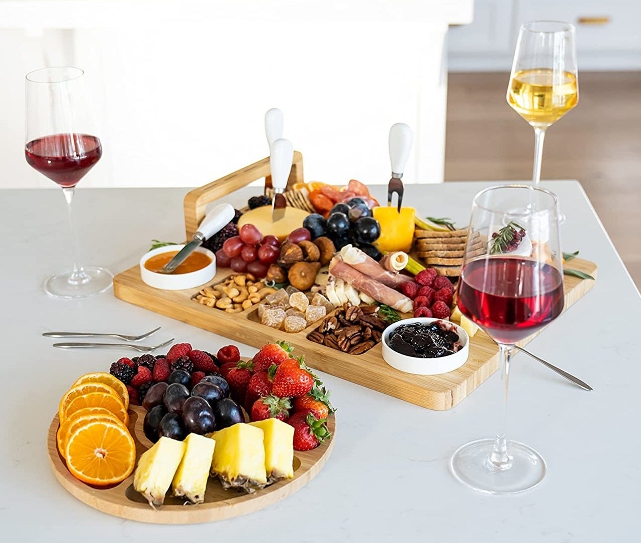 the charcuterie boards and utensils on a kitchen counter next to wine glasses