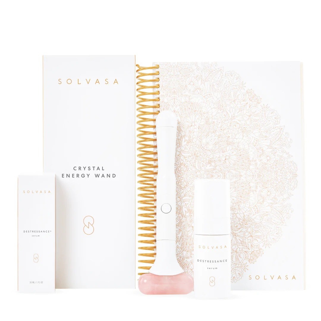 white packaged skincare products with gold accents next to white notebook.