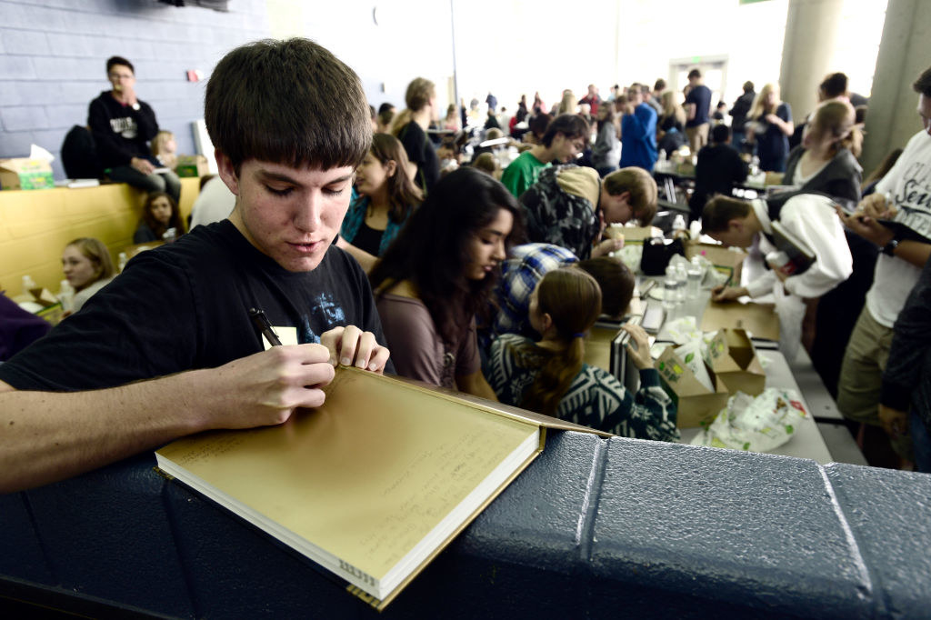 A student writing in a yearbook in a crowded room