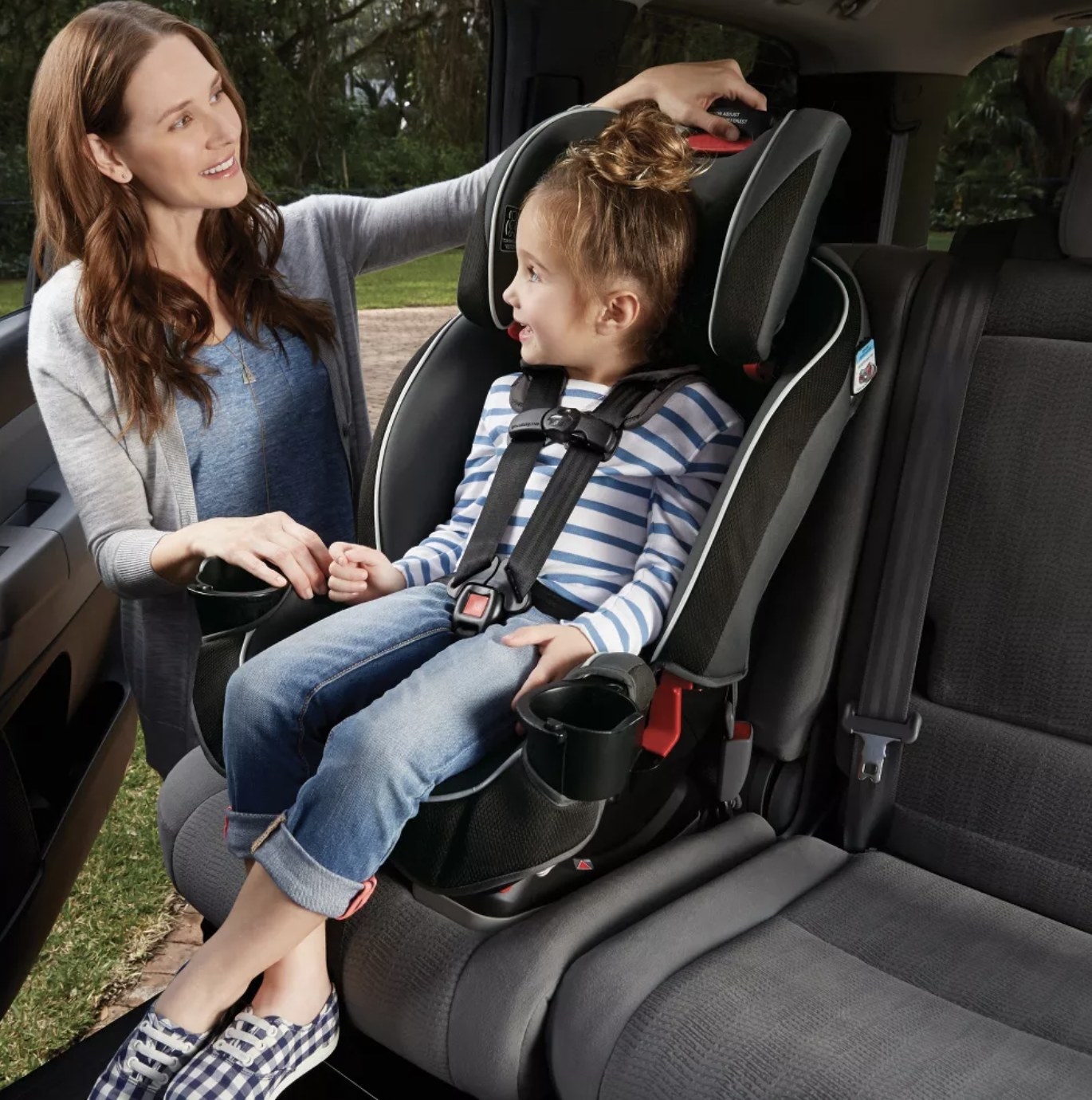 Adult buckling child into car seat with forward-facing harness