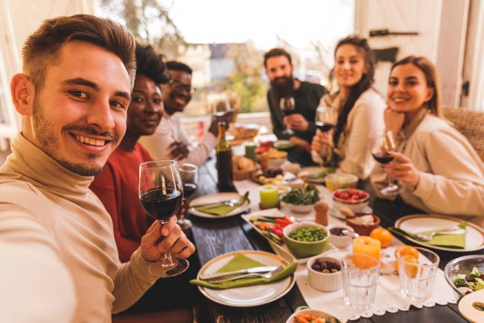Point of view shot of diverse group of friends taking selfies while sitting at the dining table and having Thanksgiving meal together. They are all looking and smiling at camera