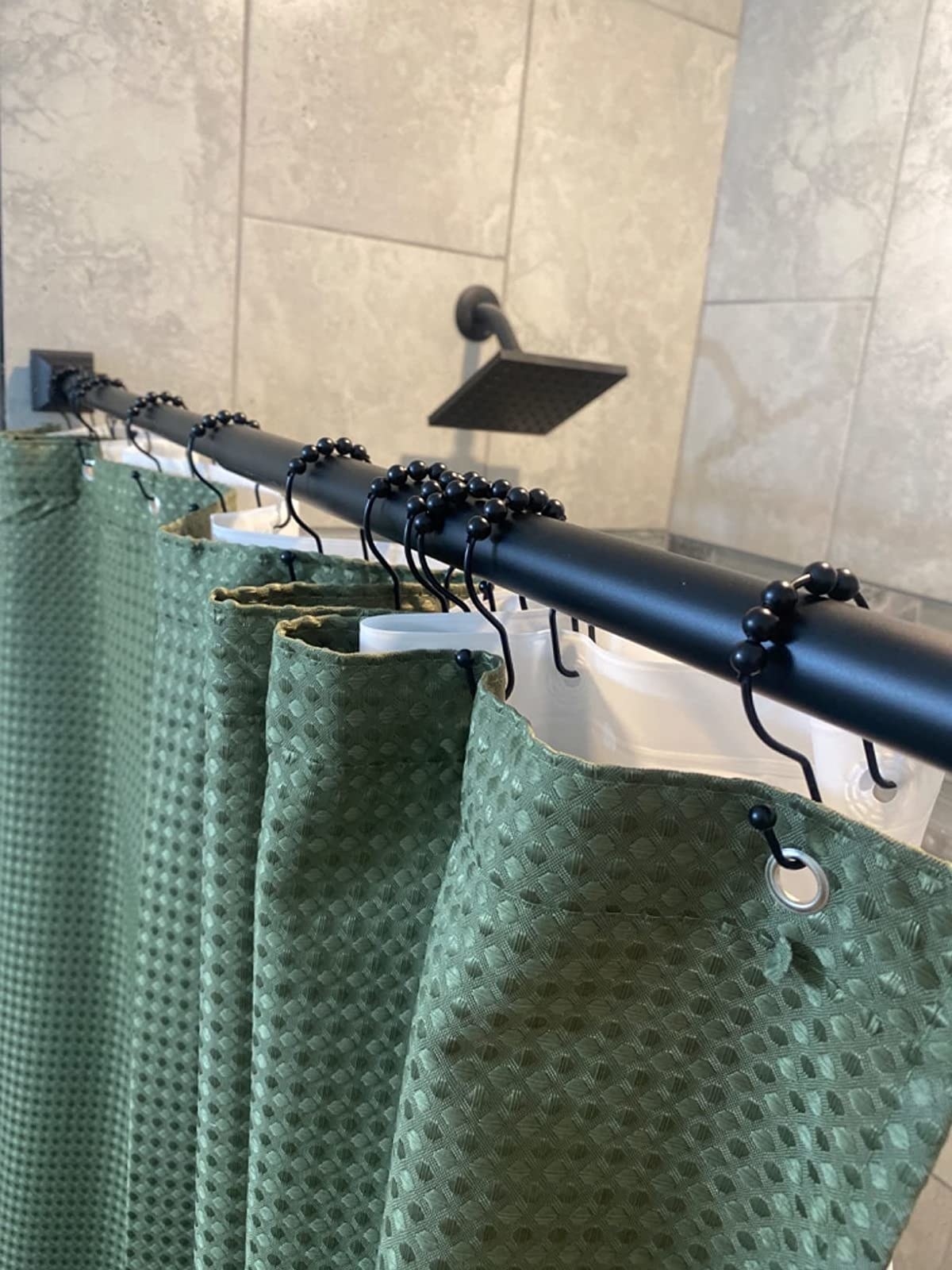 a reviewer photo of the dark dual hooks holding a green shower curtain and white liner