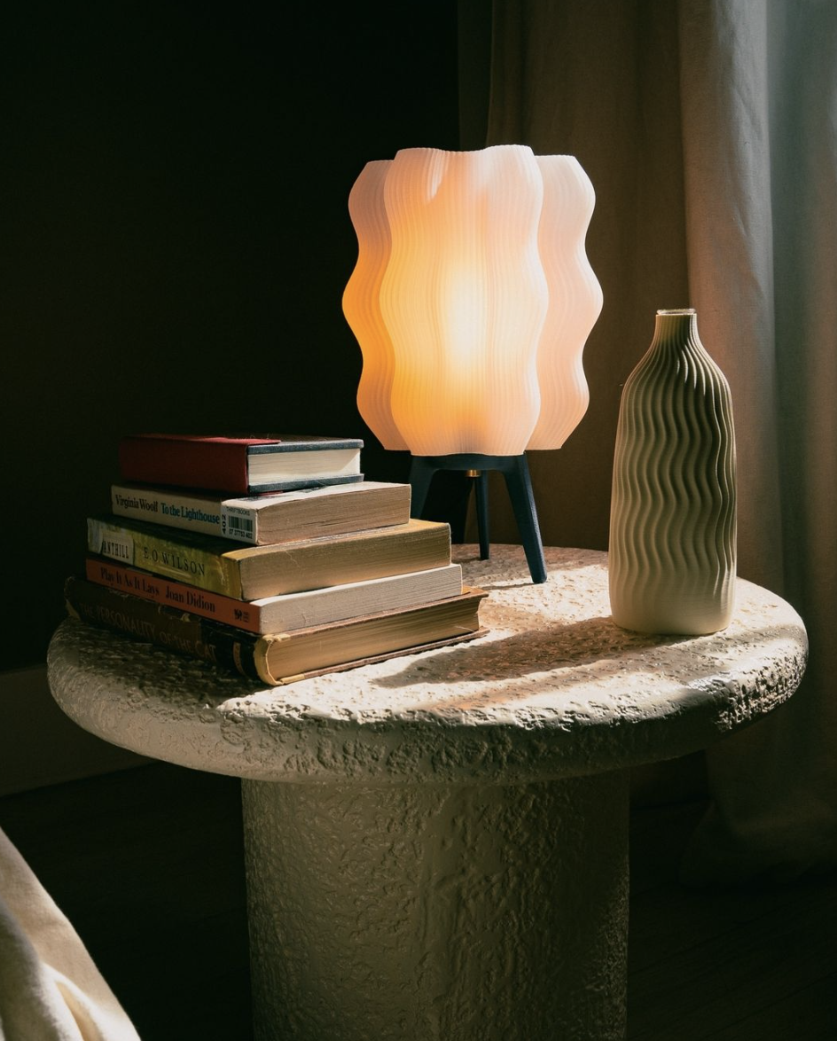 white Wavy Lamp next to stack of books and unique vase on a table.