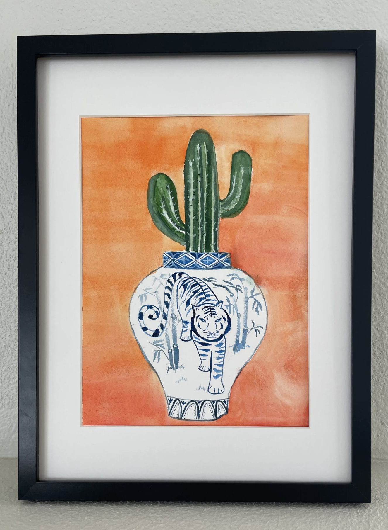watercolor painting of a cactus inside a vase showing a tiger in black frame.