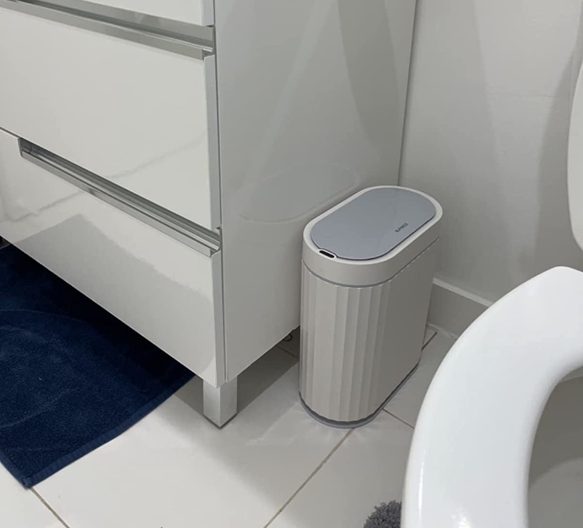 a reviewer photo of the small white trash can in a white bathroom