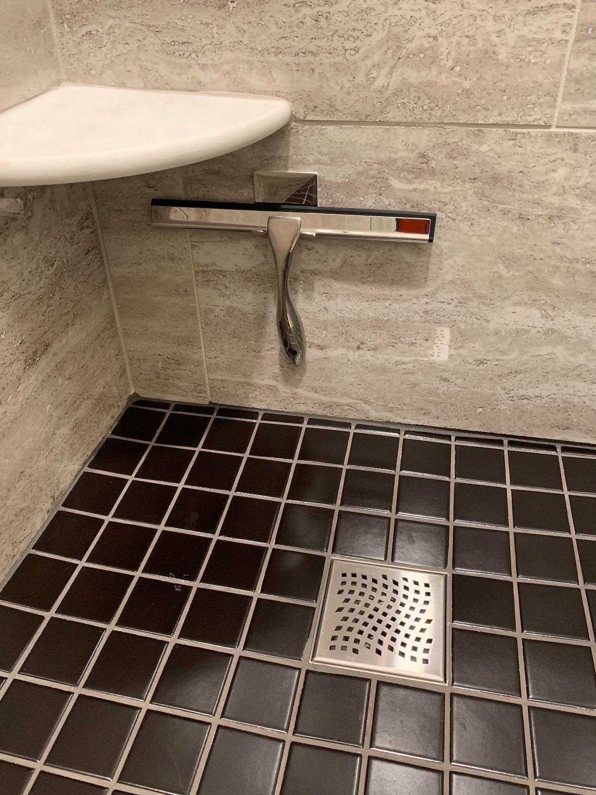 a reviewer photo of the silver squeegee hanging in a grey and black shower