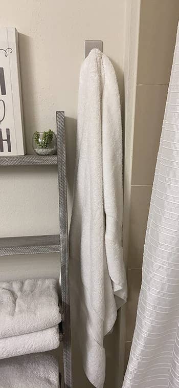 a reviewer photo of the silver hook holding a white towel in a decorated bathroom