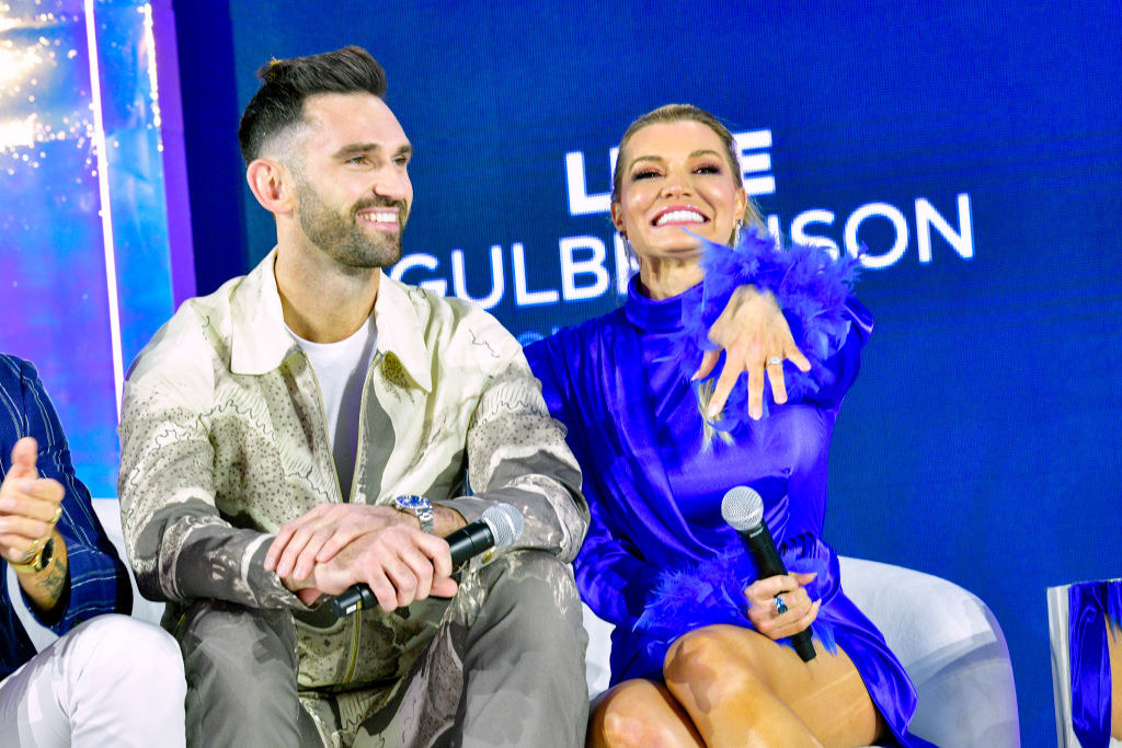 Carl smiling and sitting next to Lindsay, who&#x27;s smiling and showing off a ring
